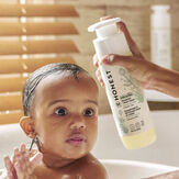 Toddler in bath with hand pouring Sensitive Shampoo + Body Wash onto toddler's head