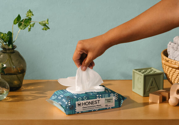 Packet of Honest's Clean Conscious Wipes placed on a diaper changing table, hand grabbing a sheet out of the package.