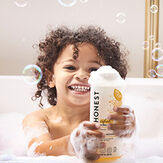 Toddler in bubble bath holding Honest bubble bath bottle