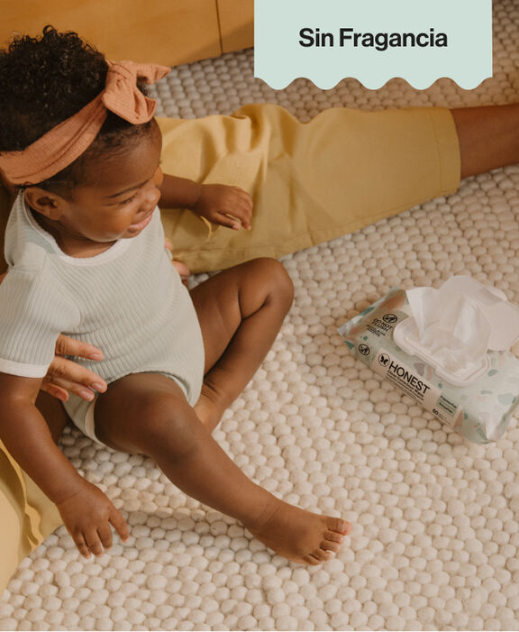 Toddler sitting on white rug next to pack of Honest Clean Conscious Wipes