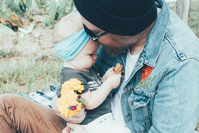 Father holding his baby girl while she plays with a flower