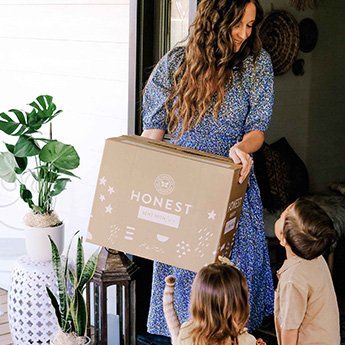 Woman holding Honest delivery box at doorway with two children
