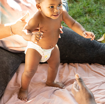 baby practicing how to walk between woman and man